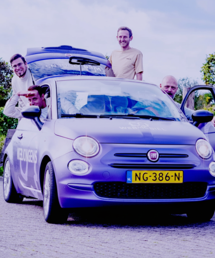 Vijf mannen poseren bij een paarse Fiat 500 met het Nederlandse kenteken NG-386-N; twee zitten in de auto, drie staan erbuiten en één houdt de autodeur open – wellicht om te praten over websites of online diensten.