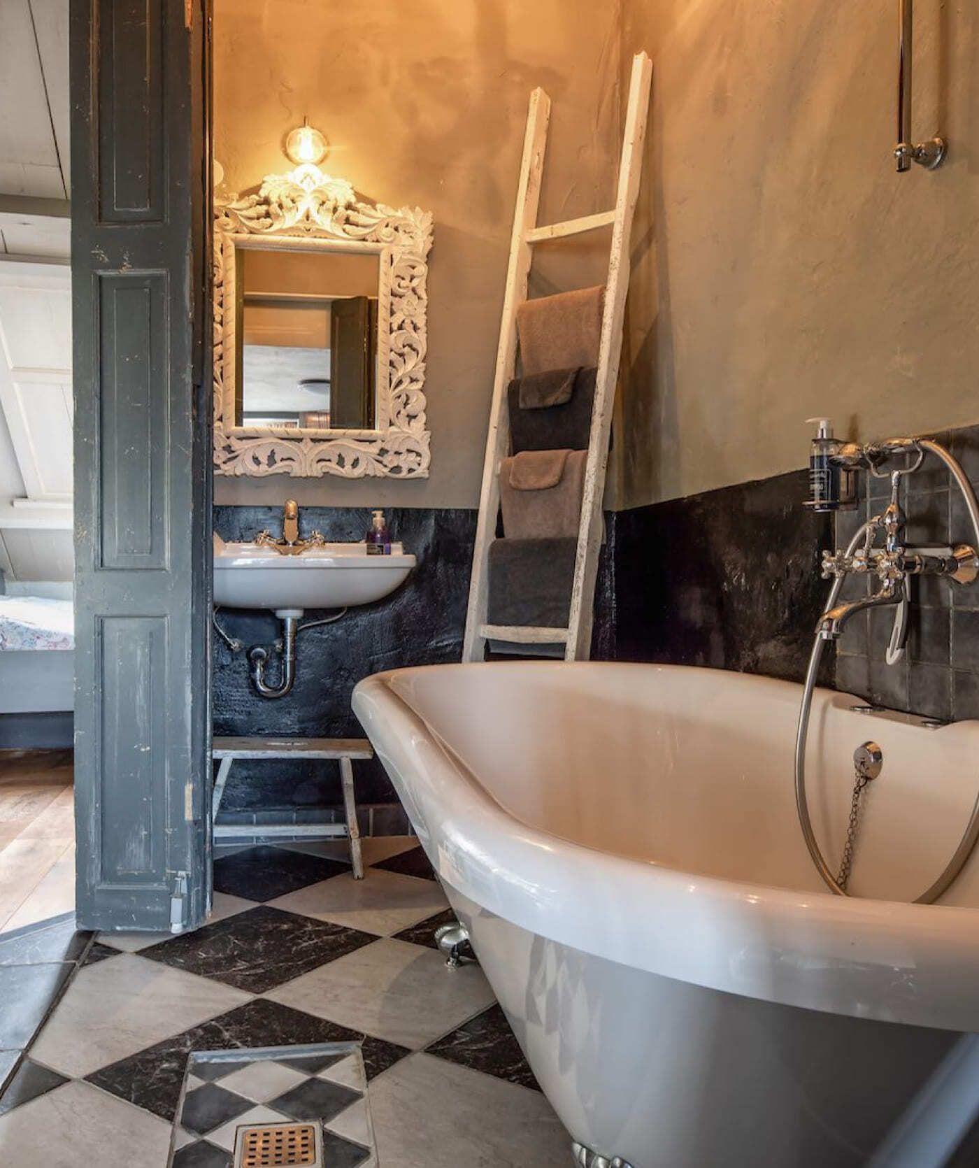 Een badkamer in vintagestijl heeft een vrijstaand bad, een wastafel met een sierlijke spiegel, een aan de muur gemonteerde kraan en een ladderplankje met handdoeken. Dit is de perfecte inspiratiebron voor websites of webshops die zich richten op interieurdesign.